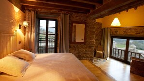 Un dormitorio con una cama grande, paredes de piedra, un balcón con vistas y techo de madera.