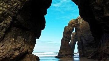 A natural rock formation with a clear sky and calm sea.