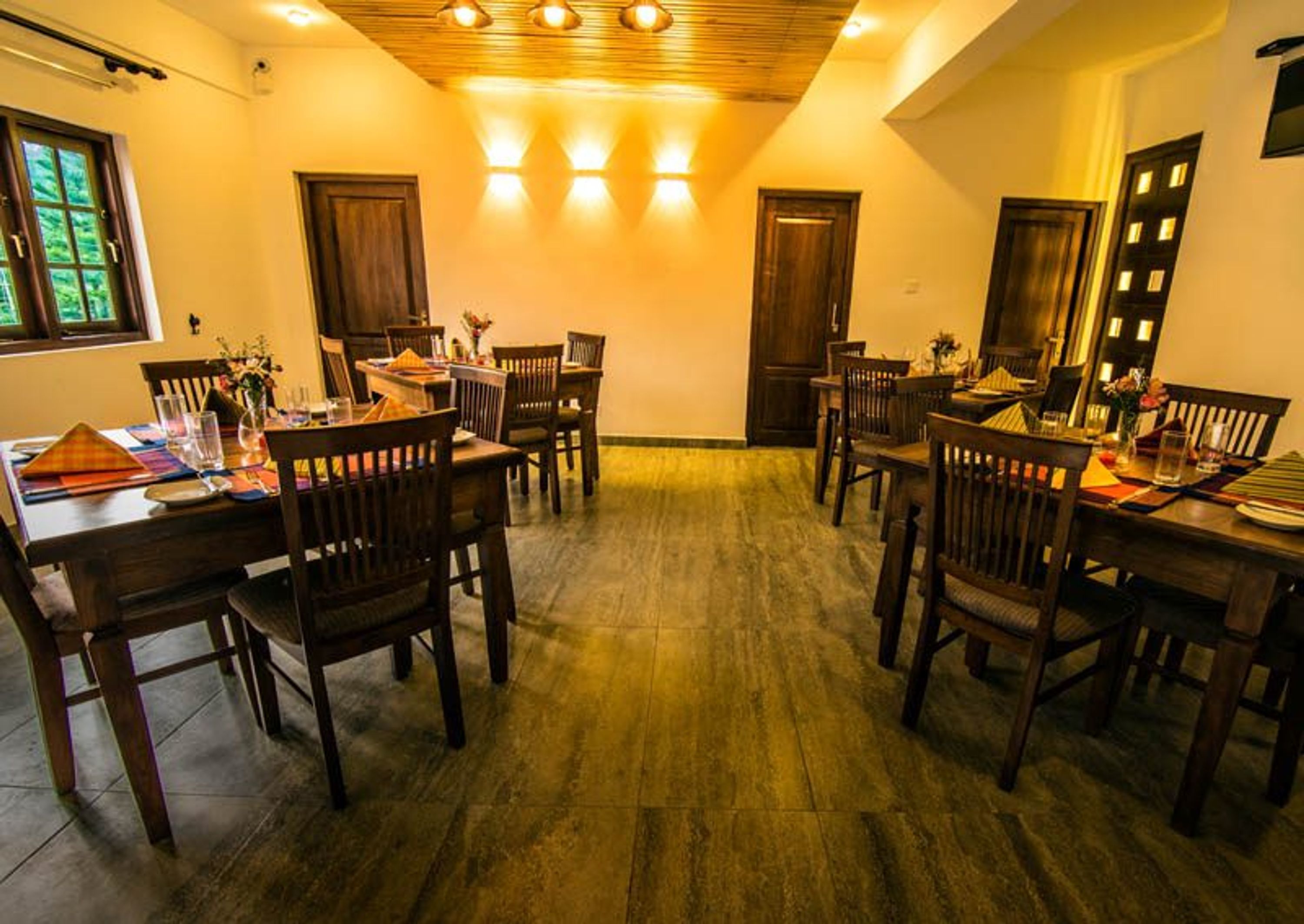 A dining area with wooden tables and chairs, a wooden ceiling, and a view of the outdoors through a window.