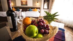 Ein Zimmer mit einem Bett, einem Nachttisch mit einer Weinflasche, einem Glas und einer Obstschale.