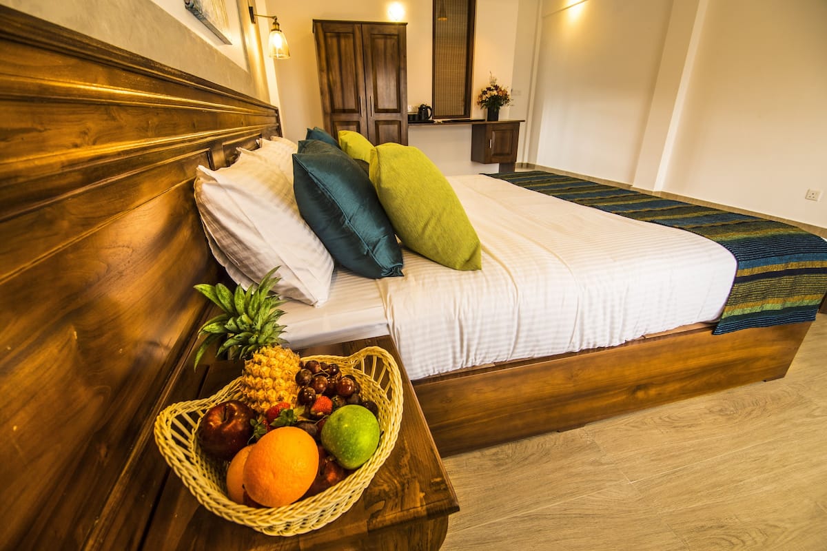 A neatly made bed with white bedding and colorful pillows, a wooden headboard, and a fruit basket on the side.