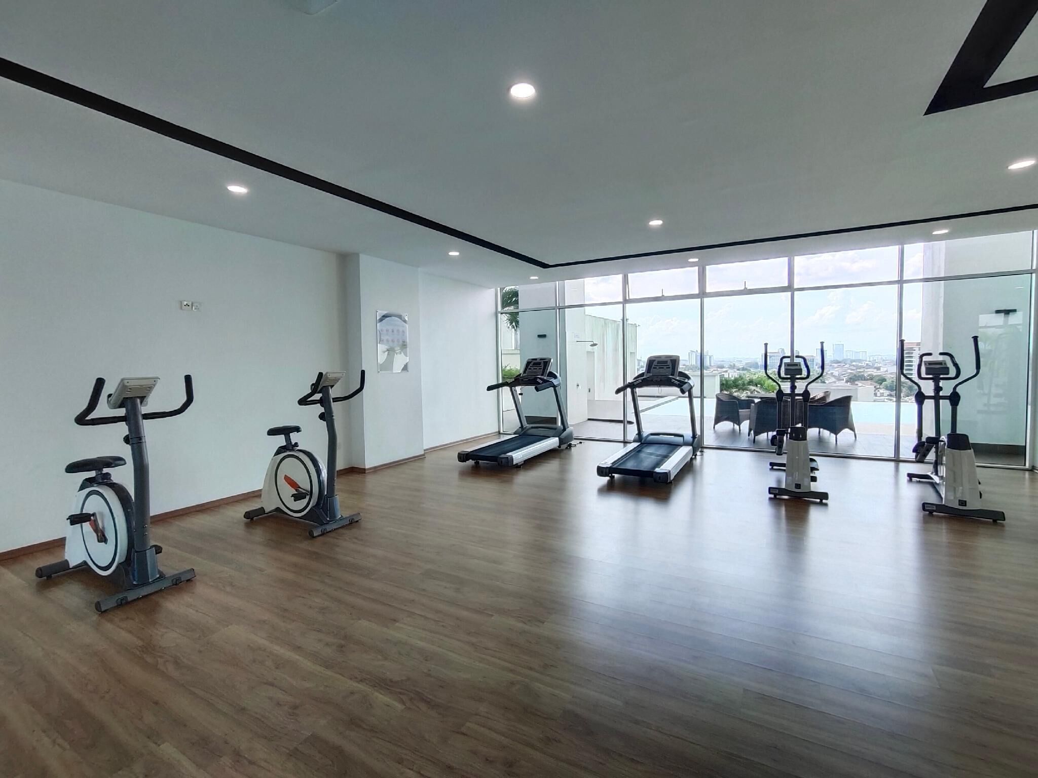 A modern gym with various exercise equipment, large windows, and a wooden floor.