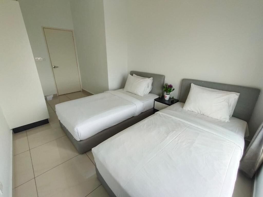 A hotel room with two single beds, a nightstand with a vase of flowers, and a door in the background.