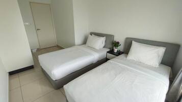 A hotel room with two single beds, a nightstand with a vase of flowers, and a door in the background.