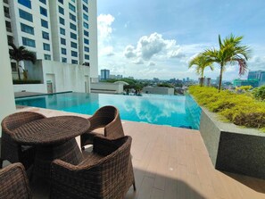 A rooftop pool area with wicker furniture and a city view.