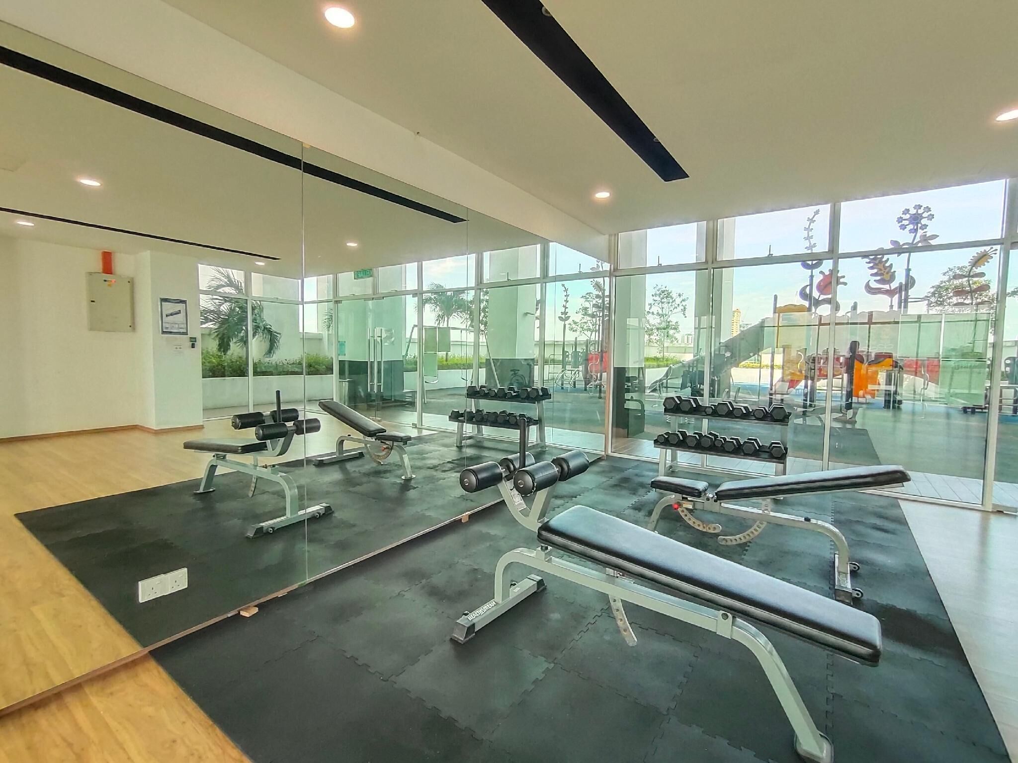 A gym with weightlifting equipment, large windows, and a view of outdoor exercise equipment.