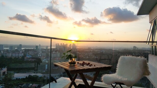 A balcony with a wooden table, a white furry chair, and a vase with a plant. - Ais Kacang Sweet Home Pinnacle Tower (Johor Bahru)