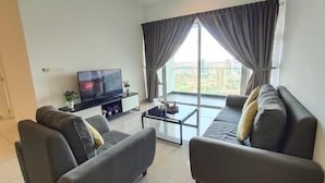 A modern living room with a flat-screen TV, grey sofas, a glass coffee table, and large windows with curtains. - Ais Kacang Sweet Home Pinnacle Tower (Johor Bahru)