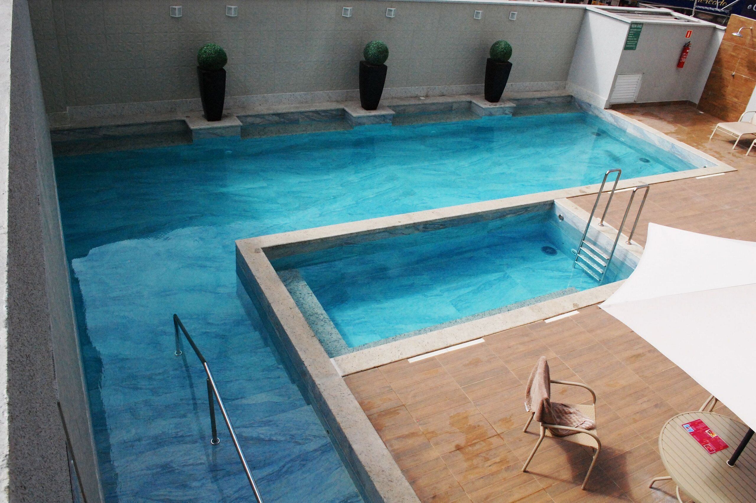 Una piscina con agua cristalina, una zona poco profunda separada y una tumbona.