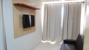 A living room with a flat-screen TV mounted on the wall, a sofa, and a window with curtains.