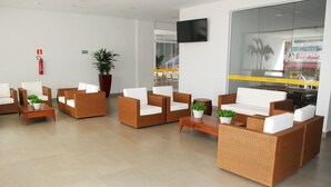 A modern lobby with wicker furniture, a flat-screen TV, and a large window overlooking a busy street.