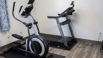 Two stationary bikes in a room with wooden flooring and a plain wall.