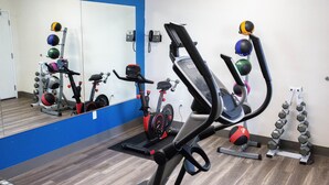 Une salle de sport équipée de matériel d’exercice, notamment un vélo d’appartement, un appareil elliptique et des haltères.