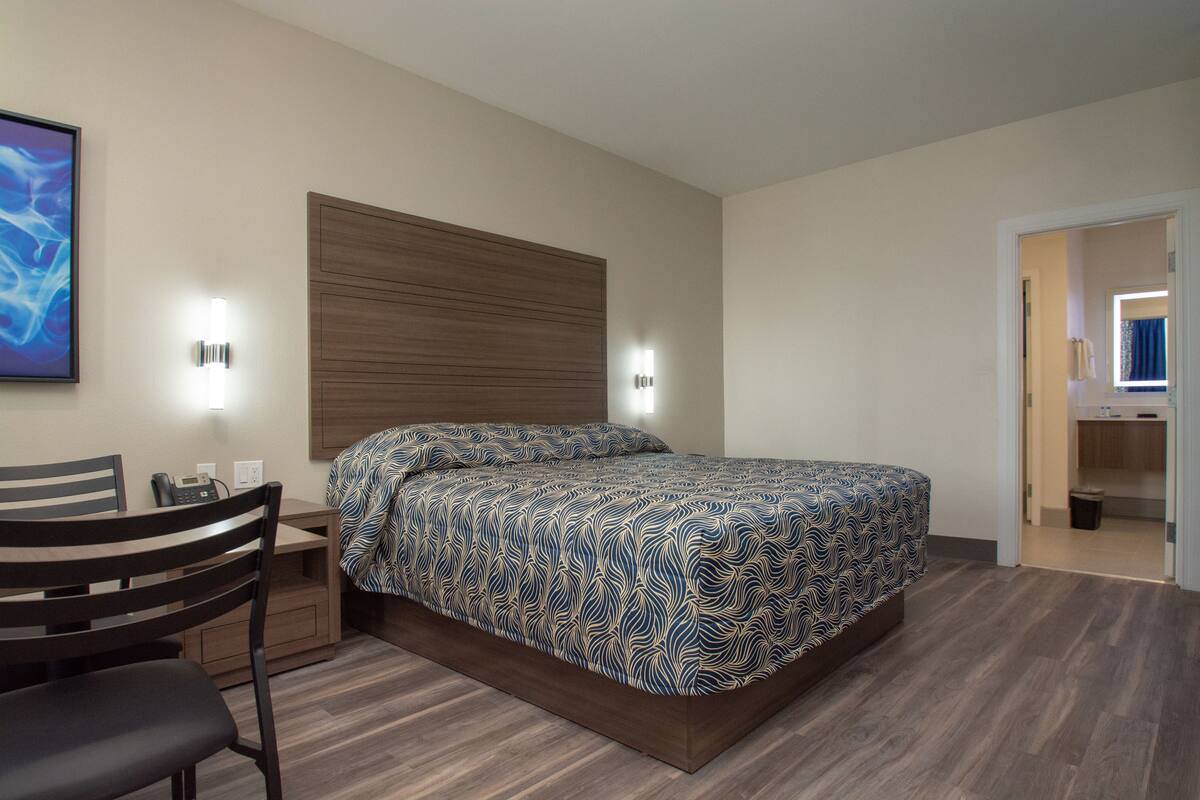 Um quarto com uma cama, uma escrivaninha, uma cadeira e uma mesa de cabeceira.