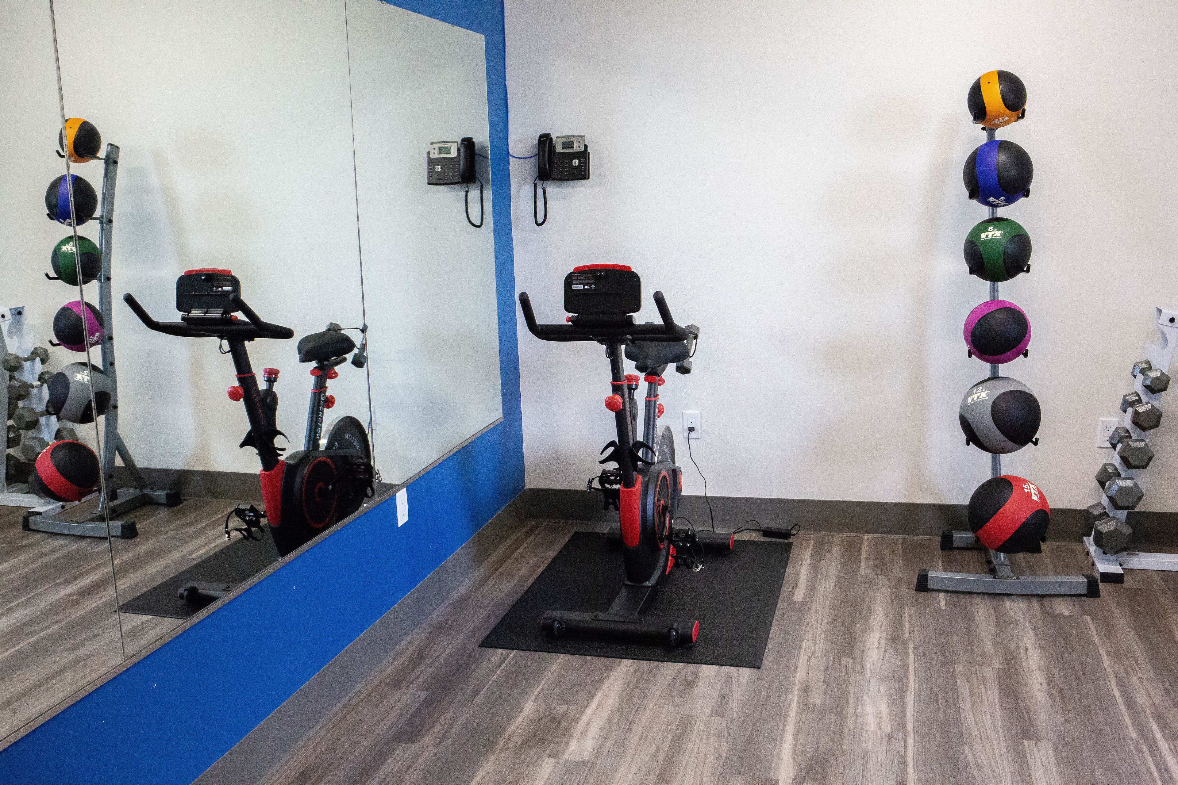 A gym with stationary bikes, a wall-mounted medicine ball rack, and a mirror reflecting the equipment.