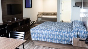 Une chambre d’hôtel comprenant un lit, un bureau, une chaise, une télévision et une salle de bain avec une baignoire, ainsi qu’une porte.