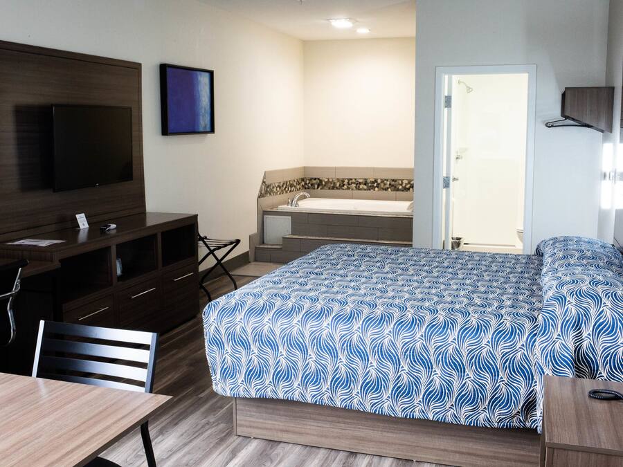A hotel room with a bed, a desk, a chair, a TV, a bathroom with a bathtub, and a door.