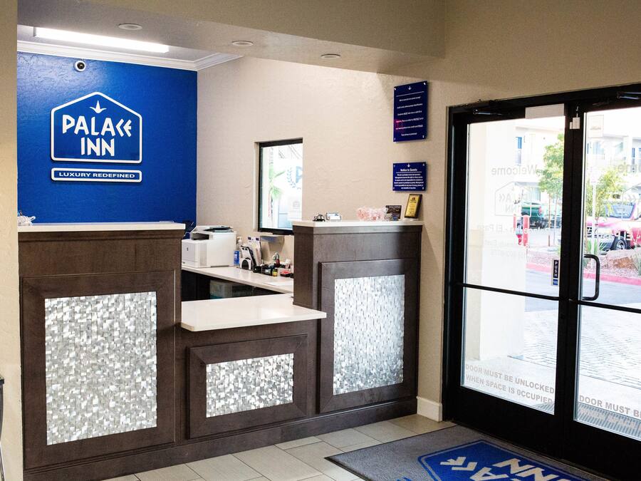 A reception area with a blue sign reading "PALACE INN LUXURY REDefined," a reception desk, a glass door with a sign, and a blue mat with "NNN" on it.