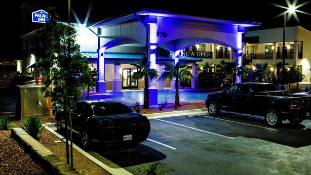 Un hôtel doté d’une entrée couverte, d’une enseigne indiquant qu’il est ouvert et d’un parking où sont stationnés deux véhicules.