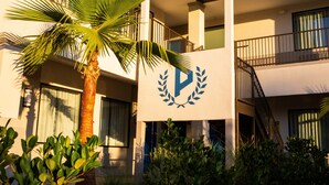 Un bâtiment moderne, avec un palmier au premier plan, des balcons et un logo sur la façade.