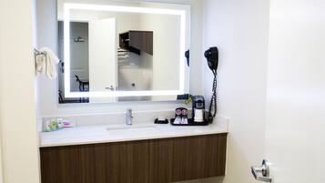Casa de banho de hotel com um espelho grande, um secador de cabelo e uma máquina de café no balcão.