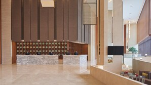 A modern lobby with a marble reception desk, a wall of circular mirrors, and a seating area with a flat-screen TV. - Four Points by Sheraton Guangdong, Heshan (Jiangmen)