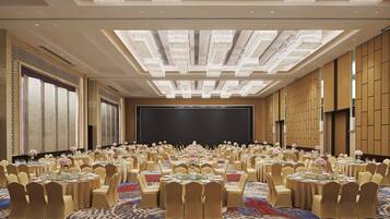 Un salón de conferencias amplio con mesas redondas, sillas color beige y una pantalla grande al frente.