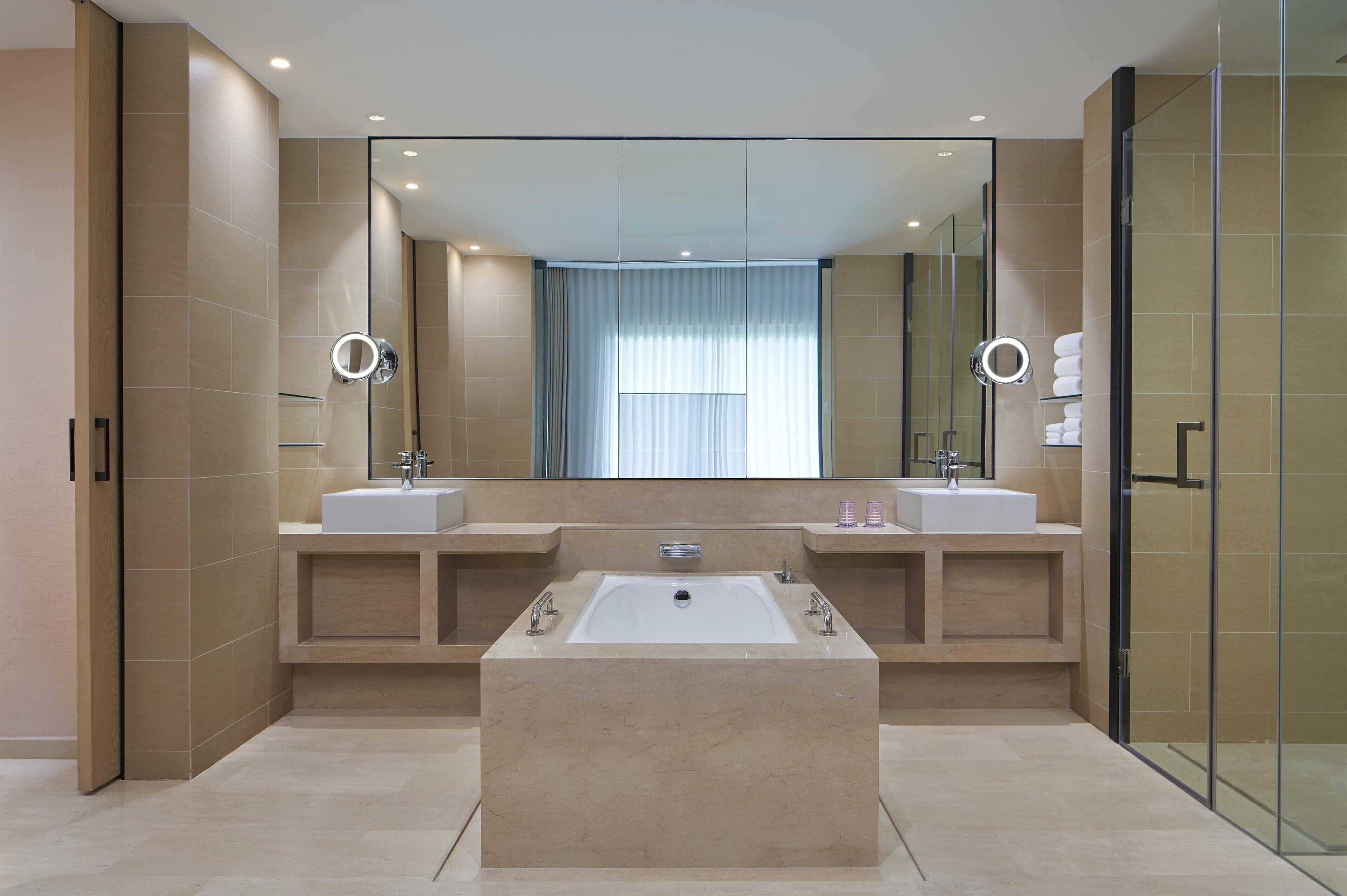A modern bathroom with two sinks, a large bathtub, and a glass shower enclosure.