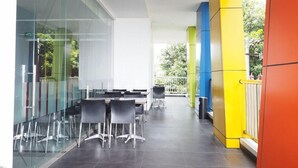 A modern indoor space with a glass wall, a meeting table with chairs, and a yellow and blue pillar. - Hotel Amaris Sriwedari Solo (Surakarta)