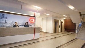 A hotel reception area with a reception desk, a staircase, and a corridor leading to elevators. - Hotel Amaris Sriwedari Solo (Surakarta)