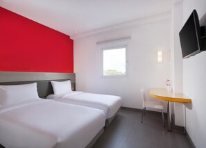 Ein Hotelzimmer mit zwei Betten, einem kleinen Tisch, einem Fernseher und einem Fenster.
