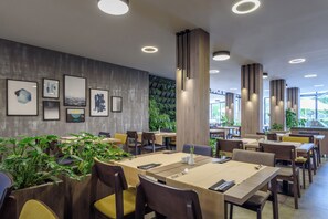 Un restaurante moderno con mesas y sillas de madera, y plantas en macetas.