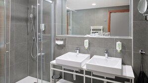 Ein modernes Badezimmer mit einer Duschkabine, zwei Waschbecken, einem Spiegel und einem Handtuchhalter.