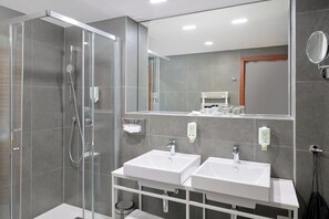 Ein modernes Badezimmer mit einer Duschkabine, zwei Waschbecken, einem Spiegel und einem Handtuchhalter.