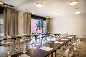 Un salón de conferencias con una larga mesa, sillas, botellas de agua y copas de vino.
