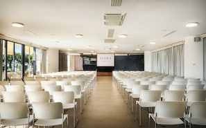 A conference room with rows of white chairs, a large screen displaying "ISTRIA ISLAND HOTEL", and a view of the outdoors through large windows. - Maistra Select Island Hotel Istra (Rovinj)