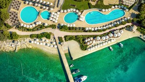 Eine Luftaufnahme eines Resorts mit zwei großen Schwimmbecken, einem Strandbereich und einer Pier mit Booten.