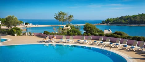 A pool with lounge chairs and a view of the sea.