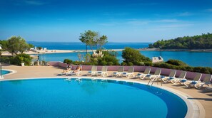 Una piscina con sillas de descanso y vista al mar.