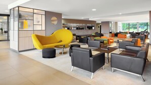 Ein moderner Lounge-Bereich mit vielfältigen Sitzmöglichkeiten, darunter ein auffälliger gelber Sessel, und im Hintergrund eine Bar.