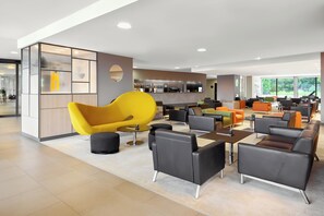 Ein moderner Lounge-Bereich mit vielfältigen Sitzmöglichkeiten, darunter ein auffälliger gelber Sessel, und im Hintergrund eine Bar.