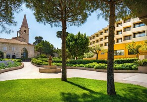 Une cour avec un clocher d’église, un bâtiment jaune et une végétation bien entretenue.
