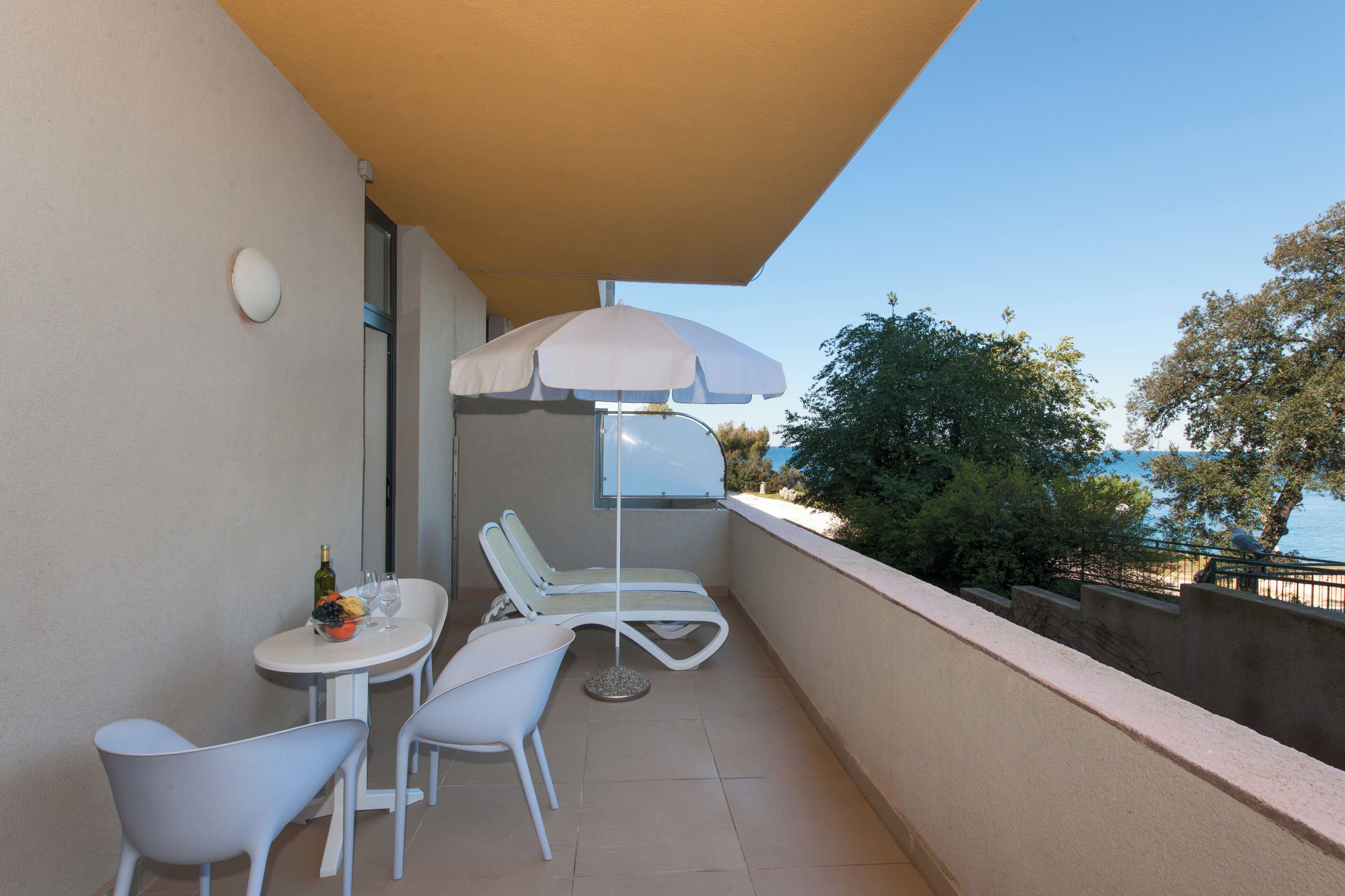 A balcony with a table, two chairs, a sun umbrella, and a bottle of wine.