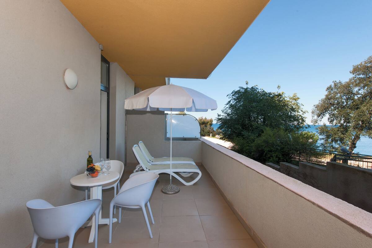 Un balcón con una mesa, dos sillas, una sombrilla y vistas al mar.