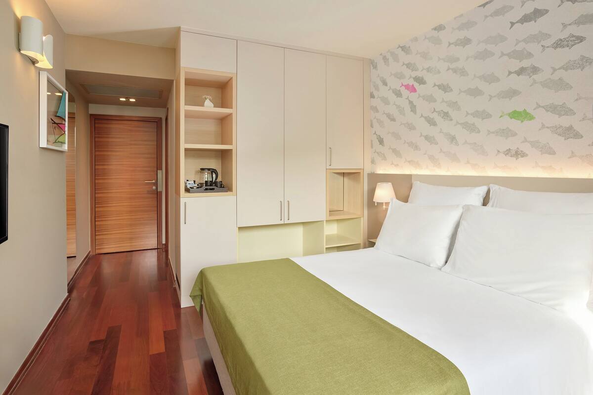 Habitación de hotel con una cama, un armario, una estantería y una pared decorada con un motivo de peces.