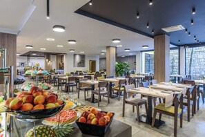 Un amplio comedor con varias mesas y sillas, una exposición de frutas y una pared de piedra al fondo.