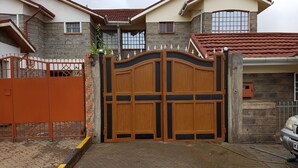 A gated entrance with a large wooden gate, a brick pathway, and a vehicle parked outside. - MJ Homestay by Balozi Nairobi (Nairobi)