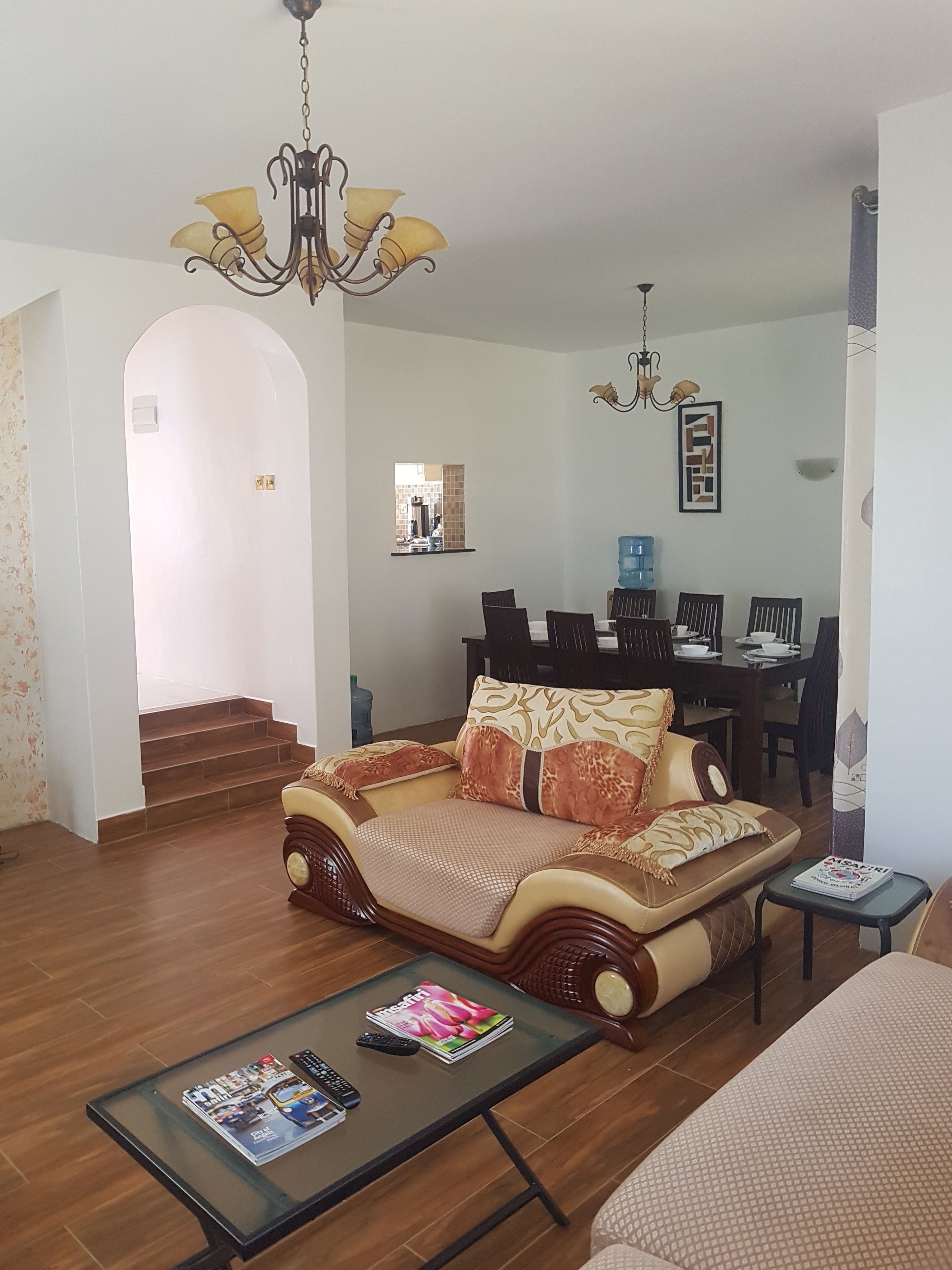 A living room with a sofa, a coffee table with magazines, a dining area with a table and chairs, and a staircase leading to another room.