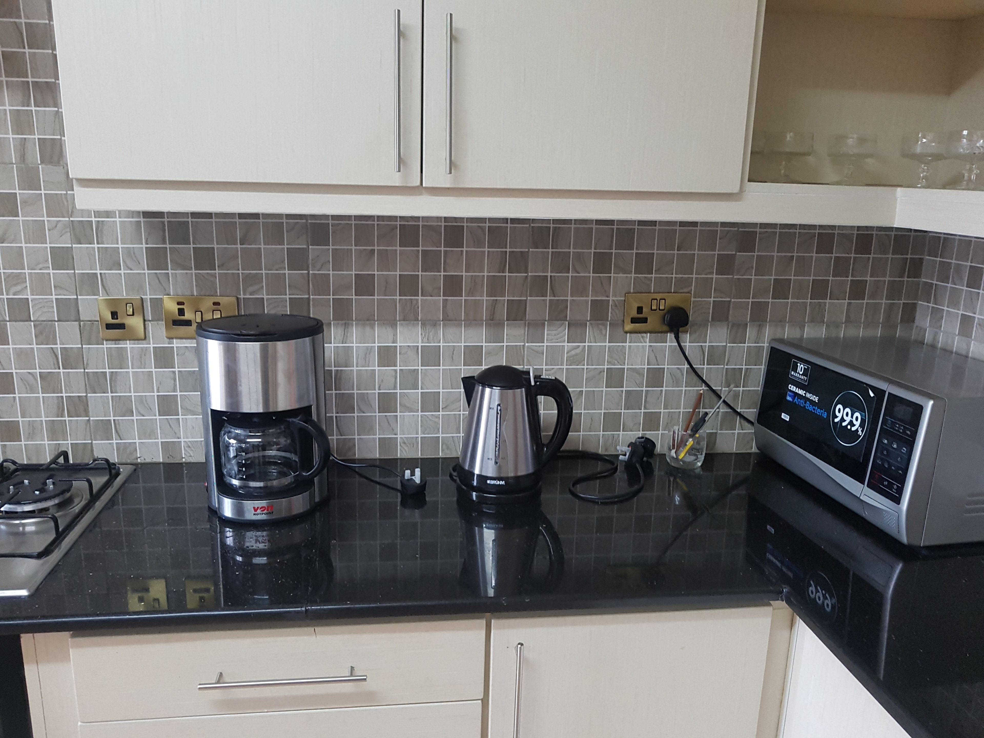 Eine Küche mit Kaffeemaschine, Wasserkocher und Mikrowelle auf einer schwarzen Arbeitsplatte.