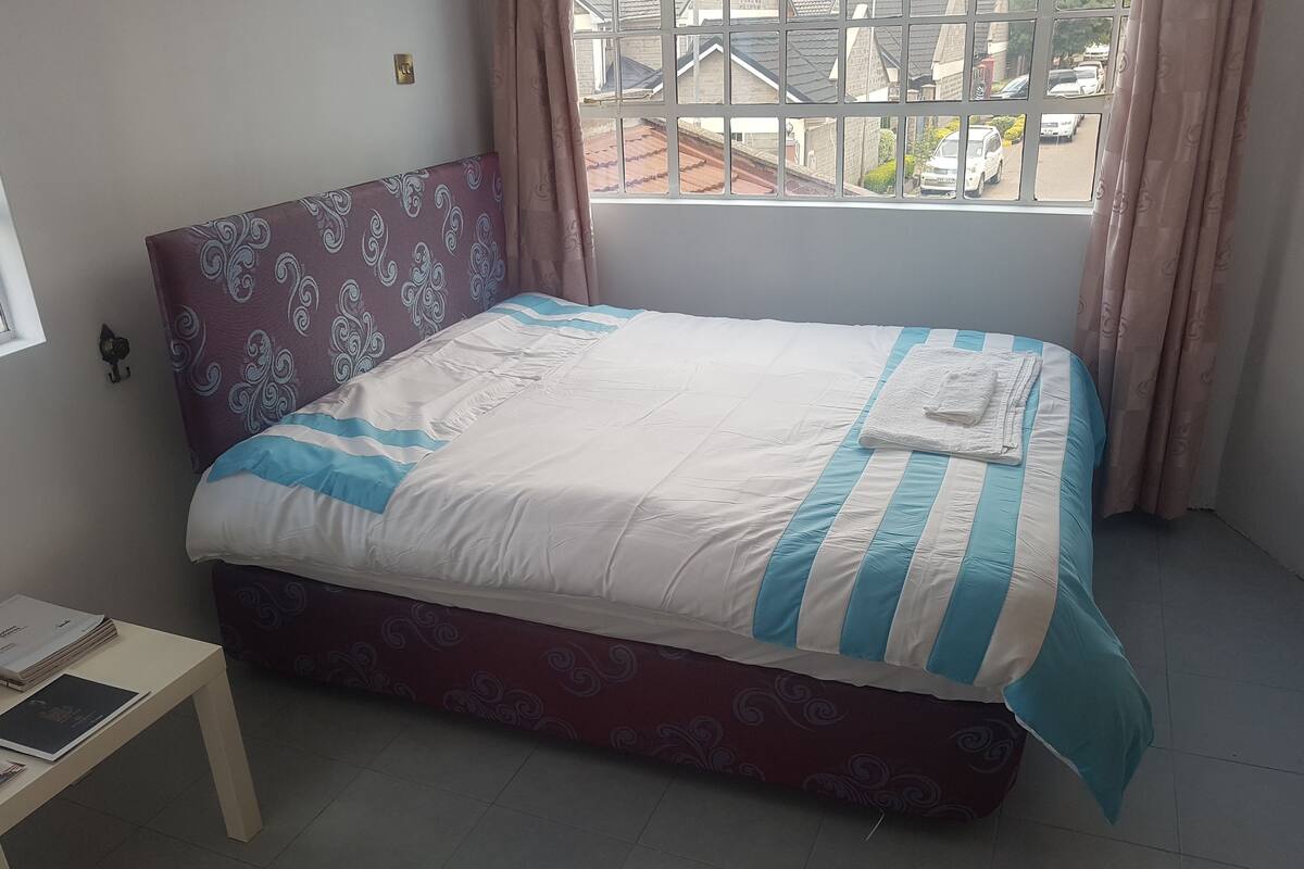 A neatly made bed with a patterned headboard and a view of the outside through a window.